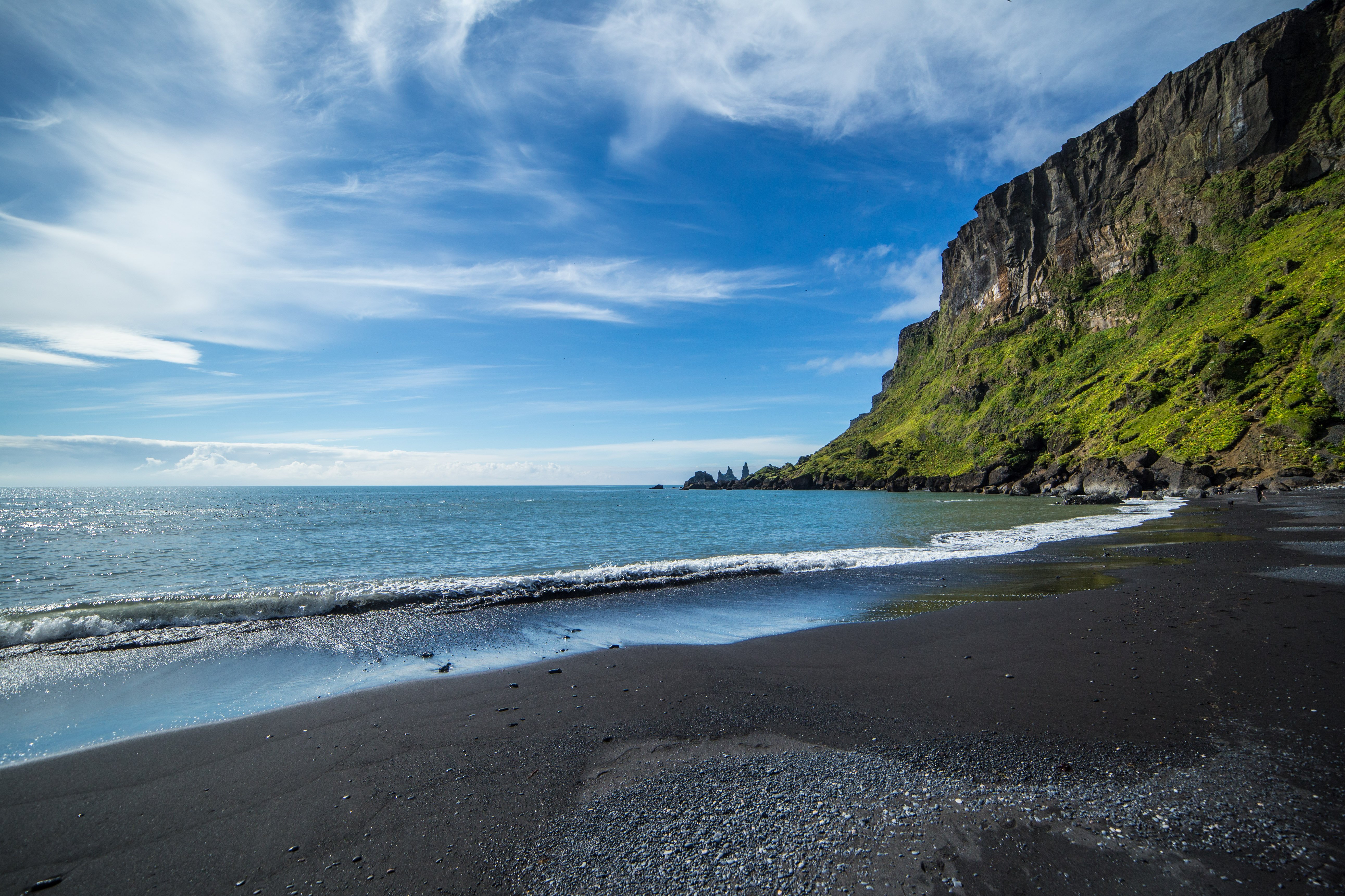 Black sands and blue sea flanked by mossy cliff on Reynisfjara Beach