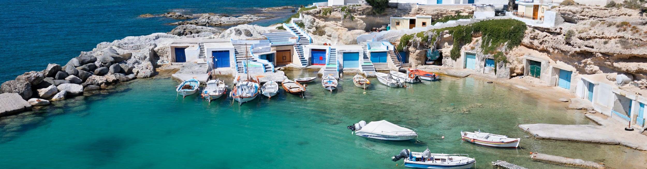 Fishing boats in a small harbour with whitewashed houses in Milos, Greece